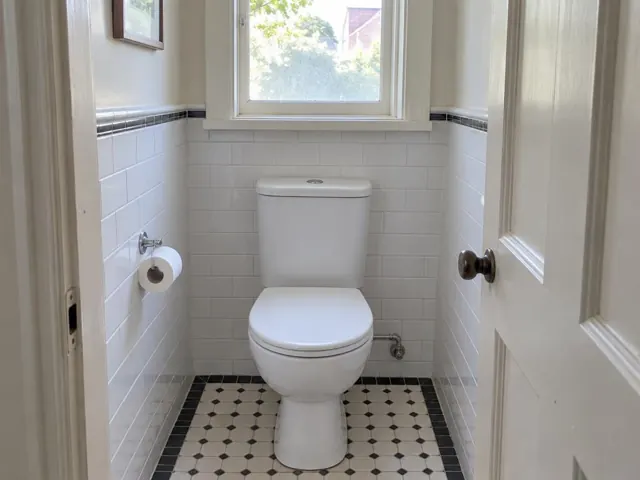 Clean white toilet in a tiled small bathroom with window and patterned floor in Newtown
